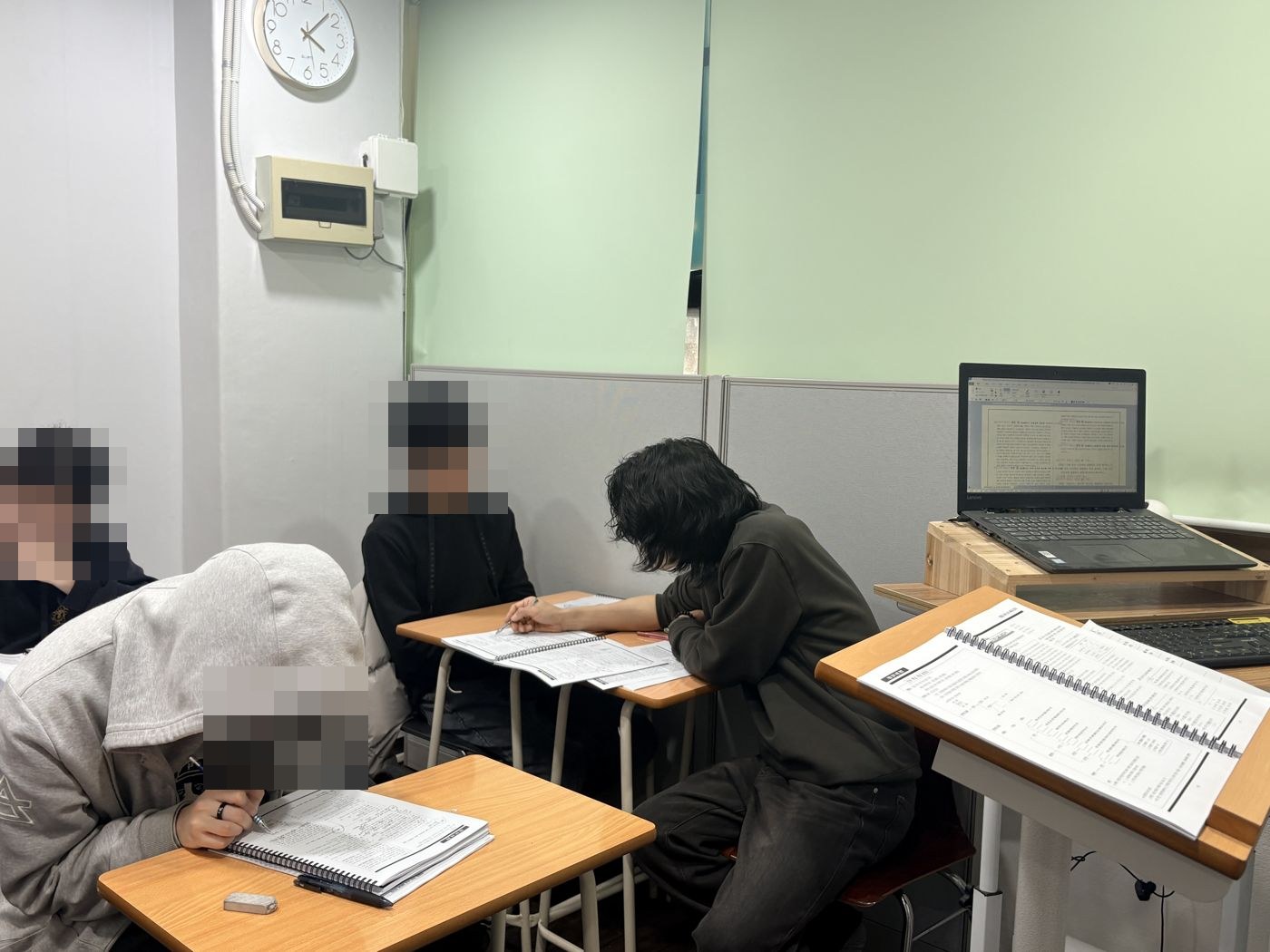 세 명이 각자 풀이하는 교실에서 원장이 한 학생 옆에 앉아 지도하는 모습